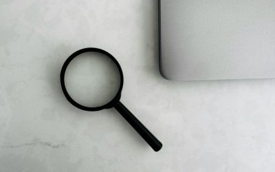 Photo by MJ Duford Magnifying glass sits near a laptop on a table